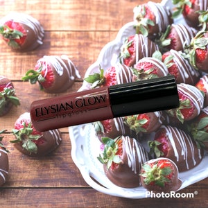 May include: A clear tube of red lip gloss with a black cap. The tube is labeled "Elysian Glow - lipgloss". The lip gloss is sitting on a plate of chocolate-covered strawberries.