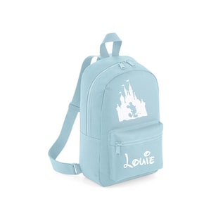 May include: A light blue backpack featuring a white silhouette of Cinderella's castle and Mickey Mouse. The backpack has a zip fastening and a white name tag that reads "Louie".