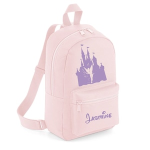 May include: Pink canvas backpack featuring a purple silhouette of a castle with a fairy flying above it. The backpack has a zipped pocket on the front and the name "Jasmine" printed below the castle.