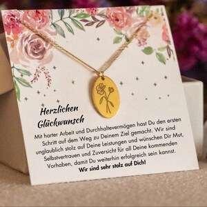 Puede incluir: Un collar dorado con un colgante floral se muestra en una tarjeta de felicitaci&oacute;n con ilustraciones florales. La tarjeta tiene el texto alem&aacute;n "Herzlichen Gl&uuml;ckwunsch". El collar est&aacute; sobre una tarjeta blanca con un dise&ntilde;o floral.