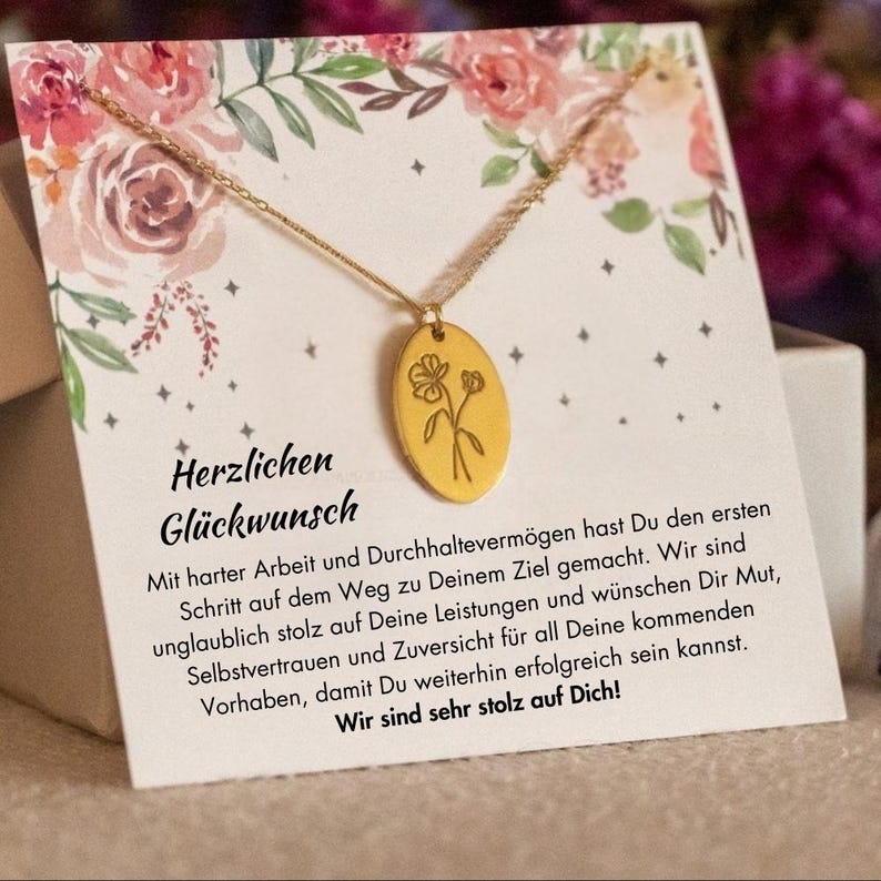 Puede incluir: Un collar dorado con un colgante floral se muestra en una tarjeta de felicitaci&oacute;n con ilustraciones florales. La tarjeta tiene el texto alem&aacute;n "Herzlichen Gl&uuml;ckwunsch". El collar est&aacute; sobre una tarjeta blanca con un dise&ntilde;o floral.