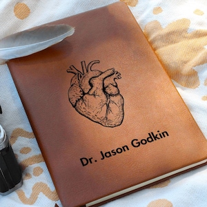 Può includere: Un diario in pelle marrone con un'illustrazione nera di un cuore anatomico e il testo "Dr. Jason Godkin" in rilievo sulla copertina.
