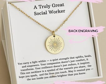 Puede incluir: Un collar dorado con un colgante redondo con un diseño de sol. El colgante cuelga de una cadena delicada. El collar se presenta en una caja de regalo blanca con el texto "A Truly Great Social Worker".
