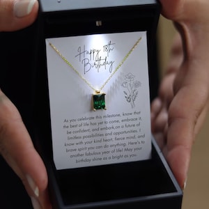 May include: A gold necklace with a green emerald pendant in a gift box. The box has a card inside with the text "Happy 18th Birthday" and a message about celebrating life's milestones.