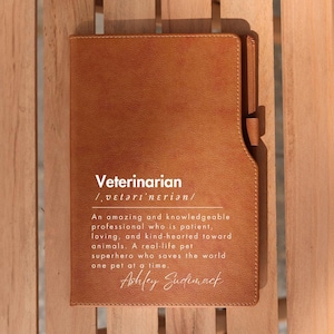 May include: A brown leather journal with the word "Veterinarian" and its definition printed in white. The journal has a white inscription that reads "Ashley Sudiomack".