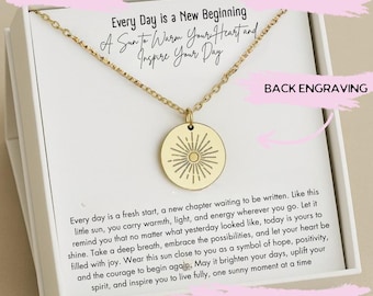 Puede incluir: Collar dorado con un colgante redondo con un diseño de sol radiante. La cadena es fina. El texto en la tarjeta dice: "Every Day is a New Beginning, A Sun to Warm Your Heart and Inspire Your Day."