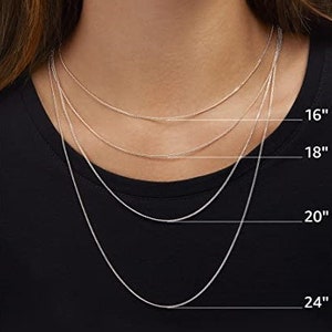 Op de afbeelding: Vier zilveren kettingen in verschillende lengtes, 16 inch, 18 inch, 20 inch en 24 inch, worden getoond op een model dat een zwart shirt draagt.