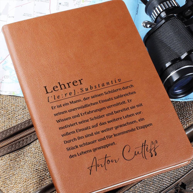 May include: A brown leather journal with the word "Lehrer" defined as a noun in German. The text describes a teacher's role in educating and preparing students for life. The journal is personalized with the name "Anton Cuttiff".