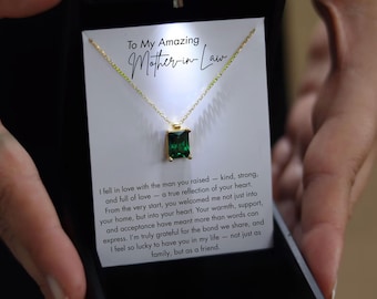 May include: A gold necklace with a rectangular, emerald-green gemstone pendant, presented in a black gift box. The card inside reads "To My Amazing Mother-in-Law" with a heartfelt message.