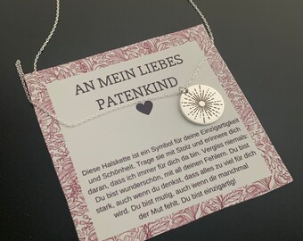 May include: A silver necklace with a small silver pendant featuring a sunburst design. The necklace is displayed on a card with the text "An mein liebes Patenkind" and a message about the necklace being a symbol of uniqueness and beauty.