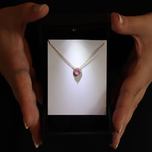 May include: A gold chain necklace with a pink heart-shaped gemstone pendant. The pendant is surrounded by smaller diamonds.