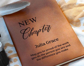 May include: A brown leather journal with the words "NEW Chapter" and "Julia Grace" engraved on the front. The journal also has the text "May you be proud of the work you do the person you are and the difference you make".