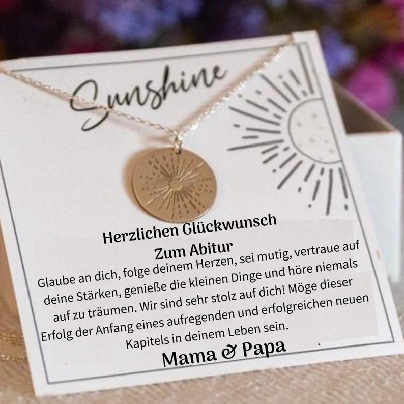May include: A silver necklace with a gold sunburst pendant. The necklace is in a white box with the words "Sunshine" and "Herzlichen Gl&uuml;ckwunsch Zum Abitur" printed on it. The text continues with a message of encouragement and support for a graduate.