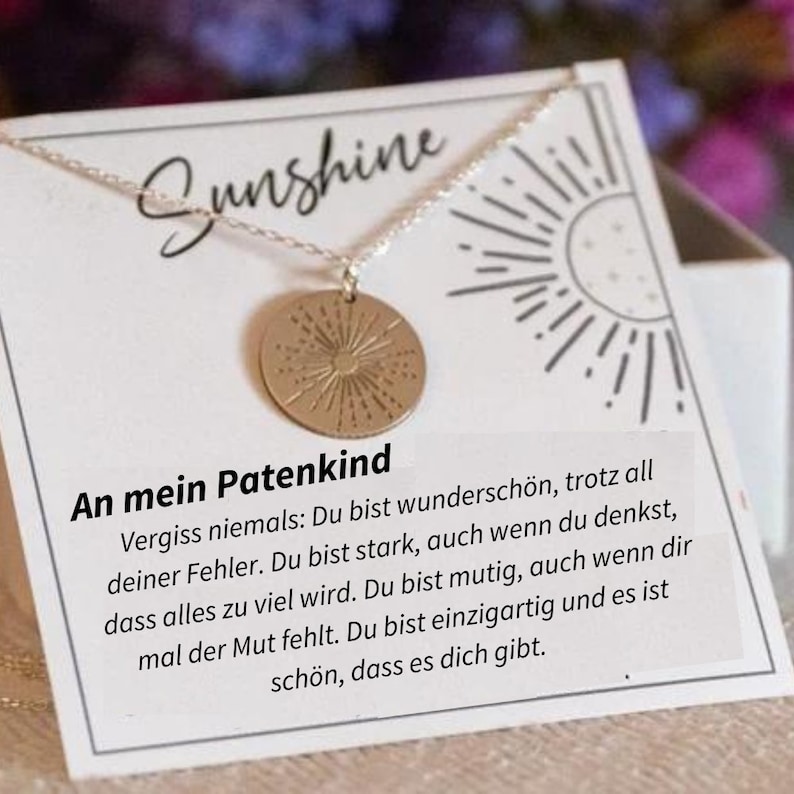 Op de afbeelding: Een zilveren ketting met een gouden zonvormige hanger. De hanger heeft een getextureerd oppervlak en een kleine cirkel in het midden. De ketting wordt getoond op een witte kaart met de tekst "Sunshine" en een boodschap over sterk en uniek zijn. De boodschap luidt: "An mein Patenkind Vergiss niemals: Du bist wundersch&ouml;n, trotz all deiner Fehler. Du bist stark, auch wenn du denkst, dass alles zu viel wird. Du bist mutig, auch wenn dir mal der Mut fehlt. Du bist einzigartig und es ist sch&ouml;n, dass es dich gibt."