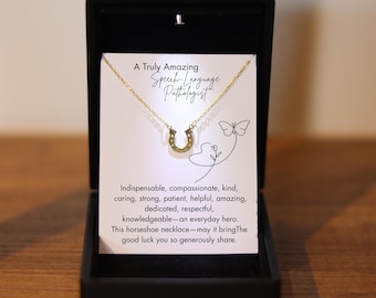 Puede incluir: Un collar de herradura dorado en una caja de regalo negra. El collar se muestra sobre una tarjeta blanca con el texto "A Truly Amazing Speech-Language Pathologist". También se incluye un mensaje sobre la buena suerte.