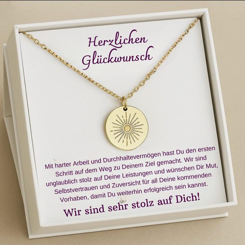 May include: A gold necklace with a round pendant featuring a sunburst design. The necklace is in a white box with a message that reads "Herzlichen Gl&uuml;ckwunsch" and "Wir sind sehr stolz auf Dich!"