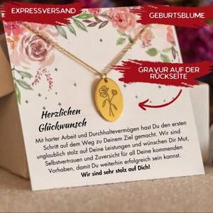 Puede incluir: Collar dorado con un colgante ovalado con un dise&ntilde;o floral, presentado en una tarjeta con decoraciones florales y texto en alem&aacute;n. La tarjeta dice "Herzlichen Gl&uuml;ckwunsch".