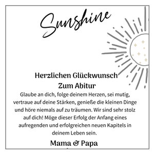 May include: A white card with a black sun graphic and the text "Sunshine" in a cursive font. The card has a message of congratulations for a graduation, with the text "Herzlichen Gl&uuml;ckwunsch Zum Abitur" and a message of encouragement. The card is signed "Mama & Papa".