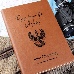 May include: A brown leather journal with the text "Rise from the Ashes" and a phoenix design. The name "Julia Chaching" is engraved below the design.