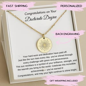 May include: A gold-colored necklace with a round pendant featuring a sunburst design. The necklace is presented in a white box with text that reads "Congratulations on Your Doctorate Degree". The image also includes text that says "Back Engraving" and "Gift Wrapping Included".