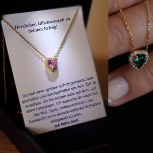 May include: A gold necklace with a heart pendant featuring a pink gemstone. The necklace is displayed in a black box with a card that reads "Herzlichen Glückwunsch zu deinem Erfolg!"  Du hast einen großen Schritt gemacht, hart gearbeitet und durchgehalten um dein Ziel zu erreichen. Ich bin extrem stolz auf dich und deine Leistungen. Ich wünsche dir weiterhin viel Mut, Spaß, Selbstvertrauen und Zuversicht um in deinem weiteren Vorhaben erfolgreich zu sein. Ich liebe dich.