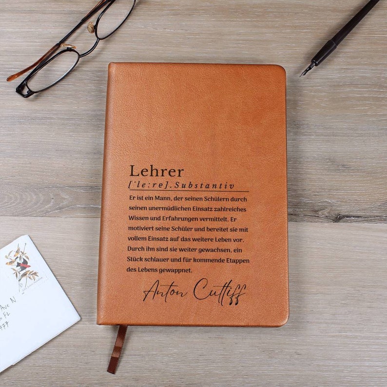 May include: A brown leather-bound journal with the word "Lehrer" (German for "Teacher") embossed on the front cover. The text below defines the word as a noun and describes the role of a teacher. The journal is personalized with the name "Anton Cuffiff" in cursive.