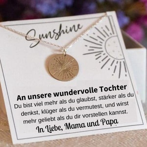 May include: A silver necklace with a gold sun pendant and a white card with the text "An unsere wundervolle Tochter Du bist viel mehr als du glaubst, st&auml;rker als du denkst, kl&uuml;ger als du vermutest, und wirst mehr geliebt als du dir vorstellen kannst. In Liebe, Mama und Papa"