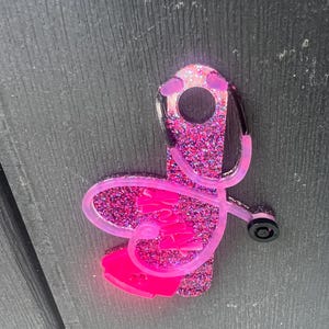 Pu&ograve; includere: Portachiavi stetoscopio con glitter rosa a forma di cuore con la scritta "Nurse" all'interno.