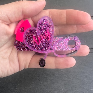 Pu&ograve; includere: Cuore glitter rosa e viola con uno stetoscopio e il nome Amy scritto al suo interno. Il cuore &egrave; attaccato a uno stetoscopio glitter rosa e viola.