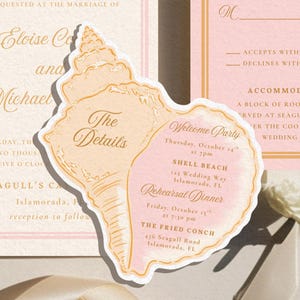 Puede incluir: Conjunto de invitaciones de boda con una tarjeta en forma de concha y dos tarjetas rectangulares. Las tarjetas tienen texto rosa y dorado. La tarjeta de concha incluye detalles del evento, y las otras tarjetas tienen información RSVP.