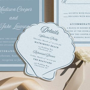 Puede incluir: Elegante juego de invitaciones de boda en tonos azules y blancos. Incluye una invitación principal, una tarjeta RSVP y una tarjeta de detalles en forma de concha. La invitación principal presenta los nombres "Madison Cooper y Jake Lawson". La tarjeta RSVP tiene espacio para una respuesta.