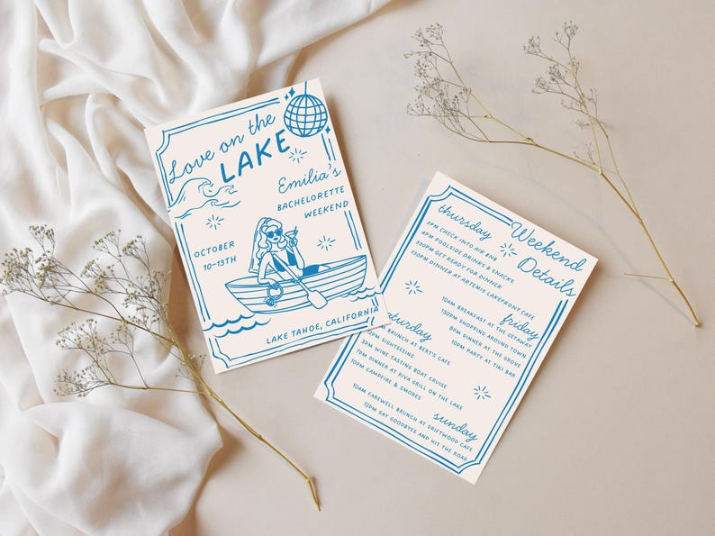 Puede incluir: Dos tarjetas de invitaci&oacute;n con texto e ilustraciones azules sobre un fondo crema. Una tarjeta dice "Love on the Lake" y "Emilia's Bachelorette Weekend". La otra tarjeta enumera los detalles del fin de semana. Flores secas y tela en el fondo.
