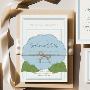 May include: Wedding invitation suite featuring a central invitation card with a light blue cloud-shaped design and the words "Welcome Party." The invitation is tied with twine and rests on a cream-colored envelope. Additional cards are visible.