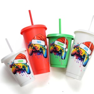 Op de afbeelding: Vier gepersonaliseerde kerstbekers met kleurrijke ontwerpen van gamecontrollers en de namen "Logan", "Theo", "Freddie" en "Jack".