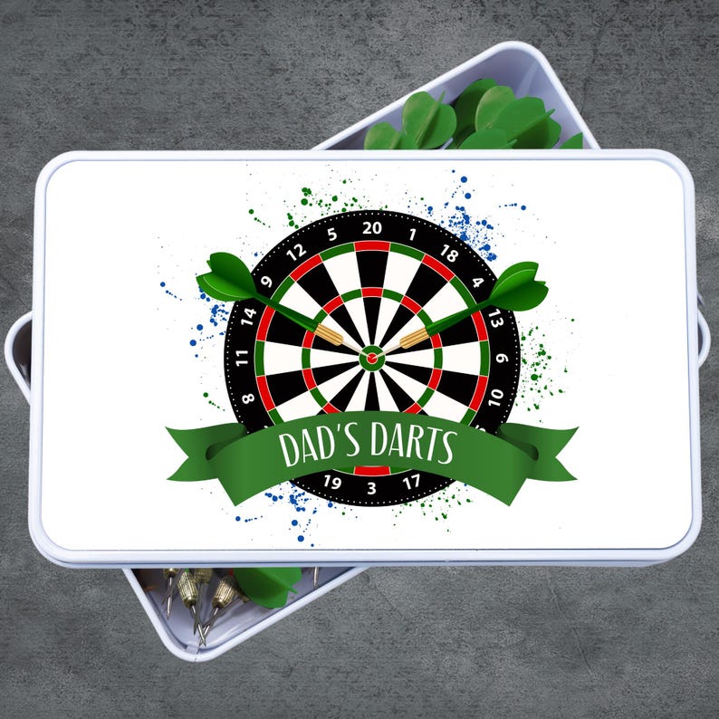 May include: White rectangular box with a dartboard design. The dartboard is black, red, and white with green darts. The text "DAD'S DARTS" is on a green banner. Blue and green paint splatters are in the background.