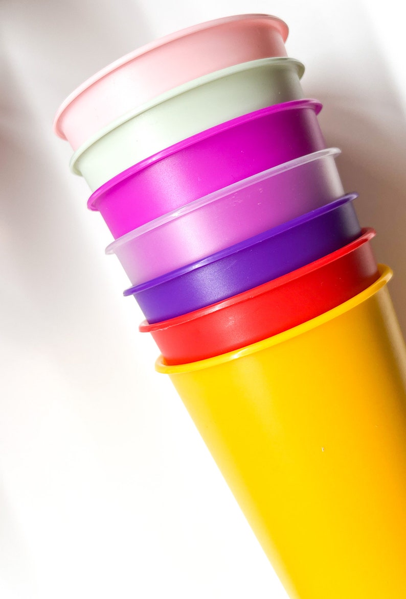 May include: A stack of six colorful plastic cups, starting with a pink cup at the top and ending with a yellow cup at the bottom. The cups are stacked in a pyramid shape.