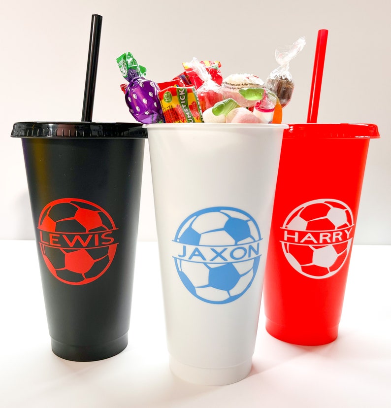 May include: Three black, white, and red reusable cups with straws. Each cup has a soccer ball design and a name: Lewis, Jaxon, and Harry.