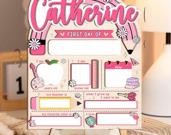 Puede incluir: Letrero de madera para el primer día de escuela con el nombre "Catherine" en rosa. El letrero incluye espacios para escribir detalles sobre el niño, como la edad, la altura, el maestro, el color favorito y lo que quiere ser de mayor.