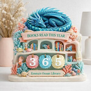 May include: A decorative bookshelf with a sleeping blue dragon on top. The bookshelf has miniature books, coral, and the text "BOOKS READ THIS YEAR." Below are three hanging tags with the numbers "365" and the text "Emma's Ocean Library."