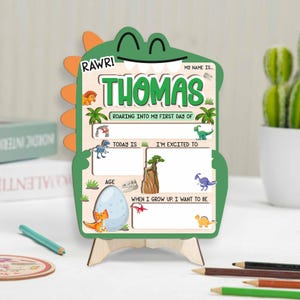 May include: A wooden dinosaur-shaped sign with the name "Thomas" in green letters. The sign has a green dinosaur head and orange spikes. It includes spaces for "Today Is," "I'm Excited To," and "When I Grow Up, I Want To Be."