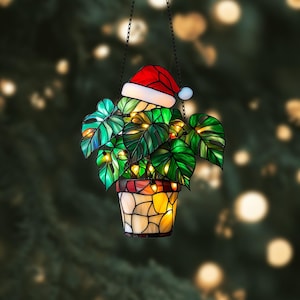 May include: A stained glass hanging ornament depicting a potted plant with green leaves and a red Santa hat. The plant is illuminated with small white lights.