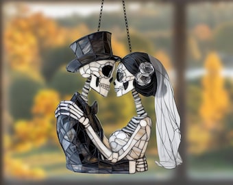 May include: A stained glass window hanging depicts a skeleton couple dressed in wedding attire. The groom wears a black suit and top hat, while the bride wears a white gown and veil. The couple are holding hands and looking at each other.