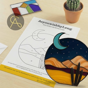 Pode incluir: Uma obra de arte em vitral retratando uma cena noturna do deserto com uma lua crescente e estrelas. A obra apresenta um design circular com uma paleta de cores de azuis, laranjas e amarelos. Um padr&atilde;o de download &eacute; vis&iacute;vel.