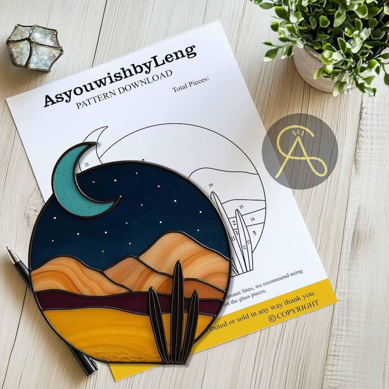 Pode incluir: Uma obra de arte circular em vitral retratando uma paisagem des&eacute;rtica com uma lua crescente, estrelas e um cacto. O design usa tons de azul, amarelo e marrom. O texto "AsyouwishbyLeng PATTERN DOWNLOAD" &eacute; vis&iacute;vel em um papel no fundo.