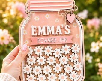 May include: A wooden reward jar shaped like a mason jar with a light pink background featuring white daisy patterns. The text EMMA'S REWARD JAR is displayed in white letters. A small wooden heart and twine bow are attached to the top right corner.