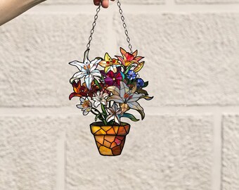 May include: A stained glass hanging decoration featuring a potted plant with colorful flowers, including lilies, in shades of white, pink, red, orange, yellow, and blue. The pot is brown and has a mosaic-like design.