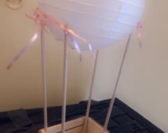 May include: A white paper lantern hot air balloon with pink ribbon accents and a pink and wood crate.