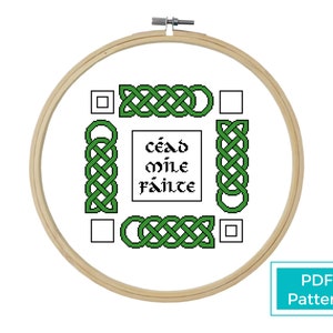 May include: A cross-stitch pattern featuring a Celtic knot design with the Irish phrase "céad míle fáilte" in the center. The pattern is displayed in a wooden embroidery hoop.