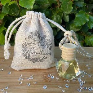 May include: A small, clear glass bottle with a wooden cap and a drawstring bag. The beige bag is printed with "Scented Creations". Decorative crystals are scattered around the bottle and bag. The bottle is filled with a yellow liquid.