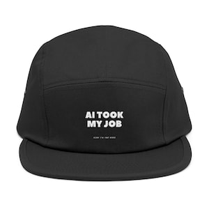 Könnte beinhalten: Schwarze Fünf-Panel-Cap mit flachem Schirm. Auf der Cap steht in weißer Schrift "AI TOOK MY JOB" über dem Text "NOW I'M THE BOSS". Hergestellt aus strapazierfähigem Stoff.